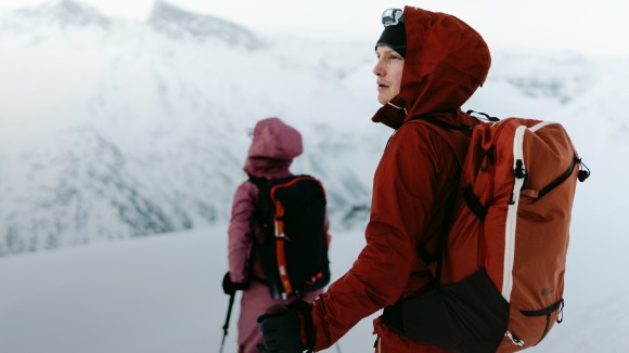 Dos personas con prendas de invierno en un paisaje montañoso con nieve.